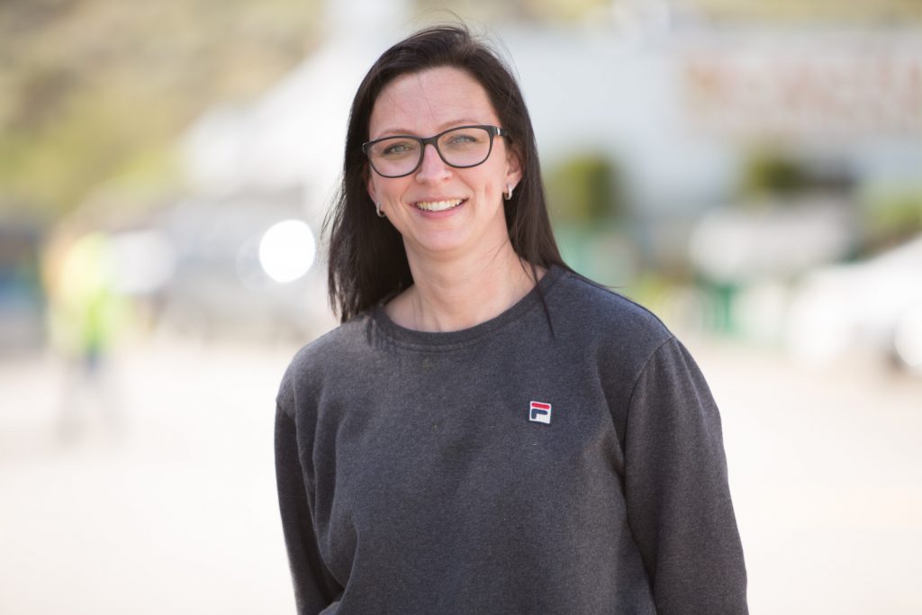 a brunette woman wearing a grey fila sweatshirt and glasses smiles at the rootze by wamaco headquarters in kamloops bc
